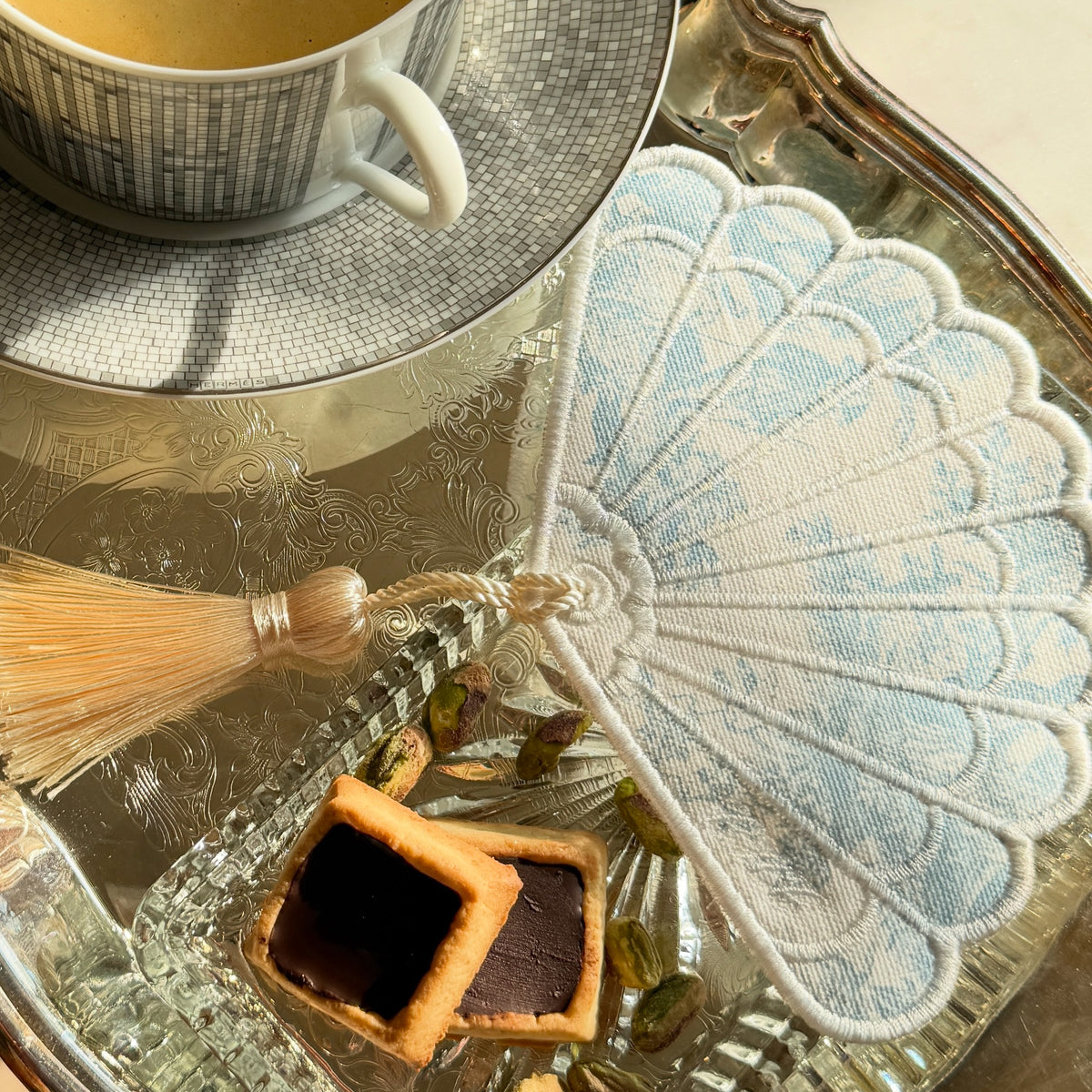 Embroidered Toile Cocktail Napkin with a fan design, beside a tea set with cookies