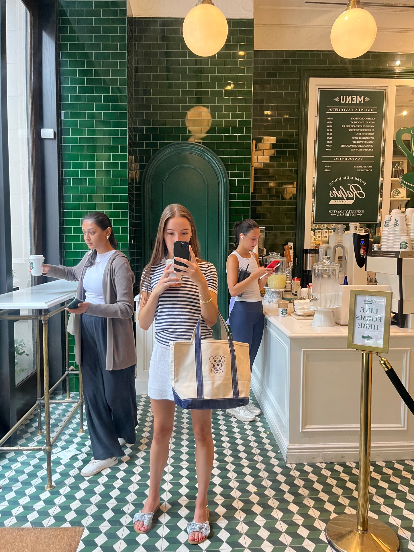 Woman taking a mirror selfie, holding a white tote bag with navy straps and an embroidered pet portrait