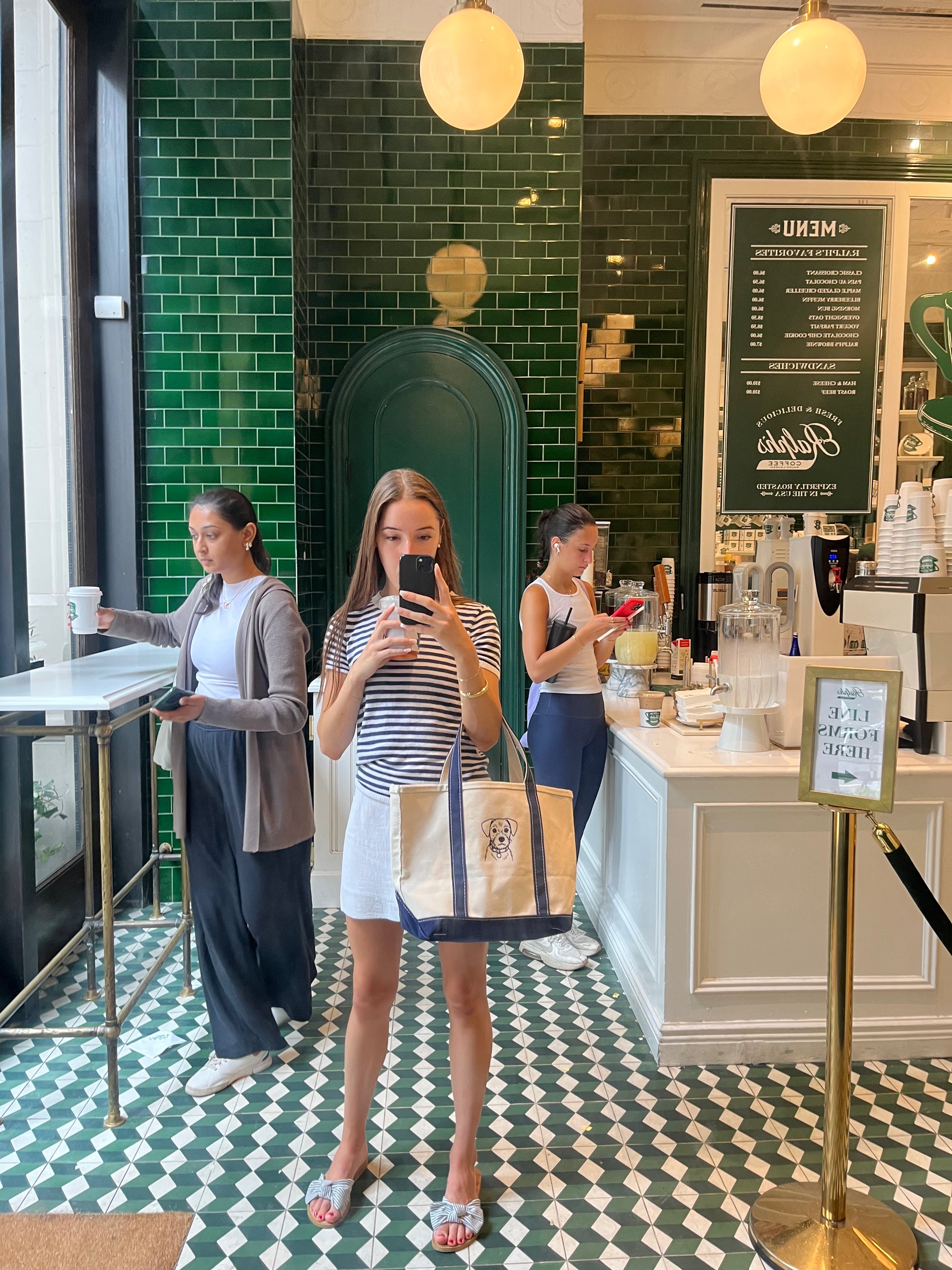 Woman taking a mirror selfie, holding a white tote bag with navy straps and an embroidered pet portrait