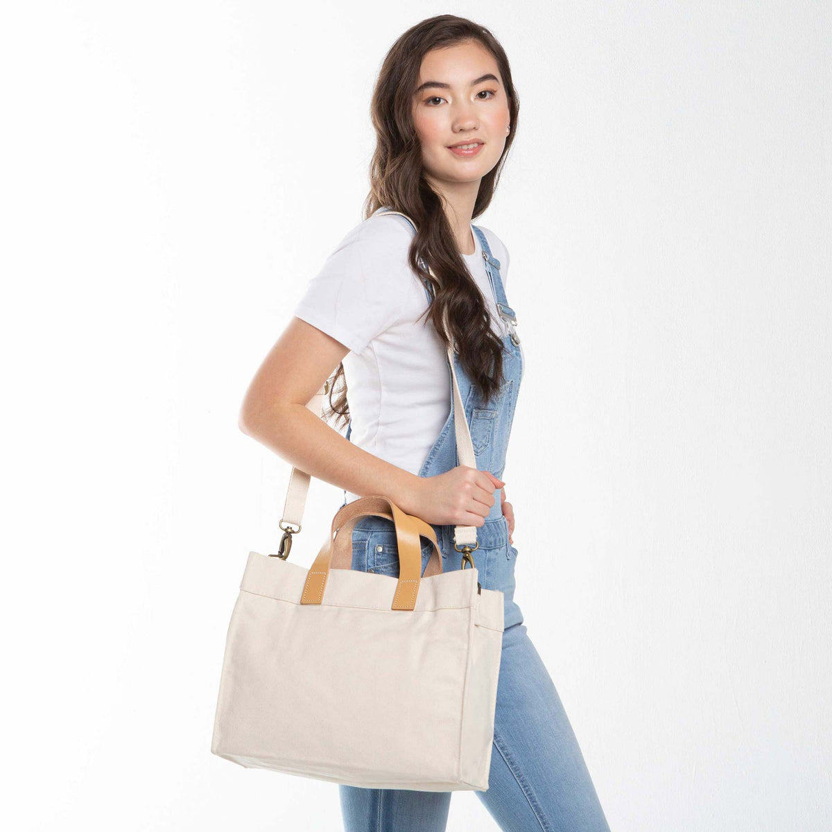 Person wearing a Crossbody White Canvas Utility Bag with Brown Leather Handles & Adjustable Strap